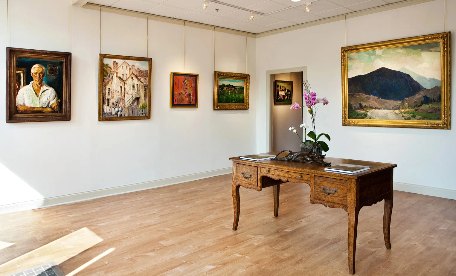 An image of a desk with orchids in a sunlit art gallery that features portraits, landscapes, and abstract art.